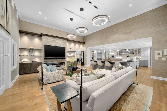 living room with a towering ceiling, a fireplace, ornamental molding, and light hardwood / wood-style floors