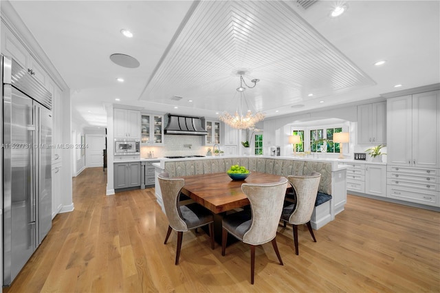 dining area with an inviting chandelier, a raised ceiling, and light wood-type flooring