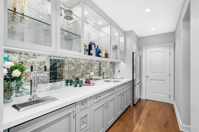 bar featuring sink, dark wood-type flooring, stainless steel fridge, gray cabinetry, and tasteful backsplash