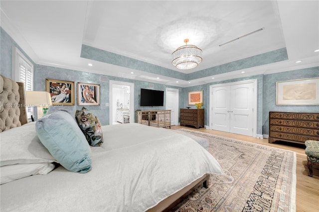 bedroom featuring an inviting chandelier, a tray ceiling, light hardwood / wood-style flooring, and ornamental molding