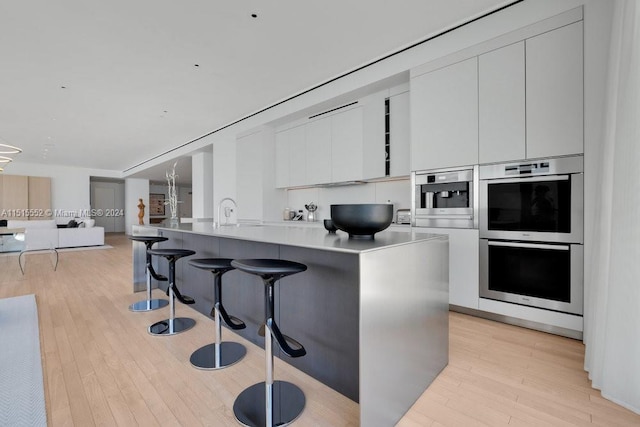 kitchen featuring a kitchen island, light hardwood / wood-style flooring, a kitchen bar, white cabinetry, and double oven