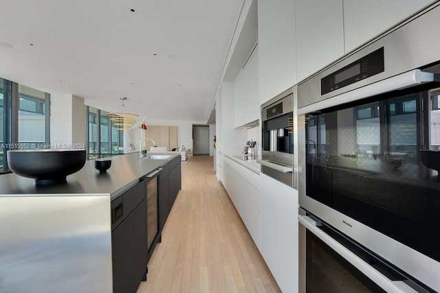 kitchen featuring pendant lighting, double oven, light hardwood / wood-style floors, sink, and white cabinets