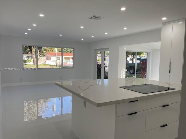 kitchen with white cabinets, black electric cooktop, light tile patterned floors, a kitchen island, and light stone counters