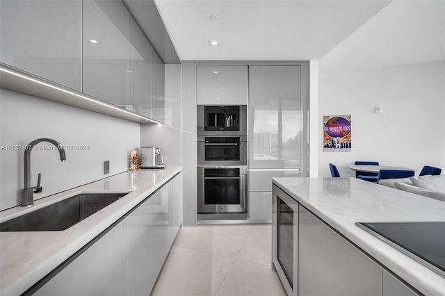 kitchen with light tile floors, light stone countertops, wine cooler, gray cabinets, and sink