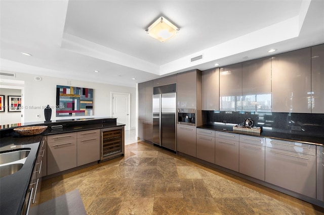 kitchen featuring tasteful backsplash, gray cabinets, wine cooler, stainless steel built in refrigerator, and a raised ceiling