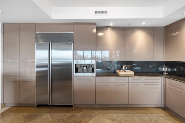 kitchen with light tile floors, stainless steel built in refrigerator, tasteful backsplash, and a tray ceiling