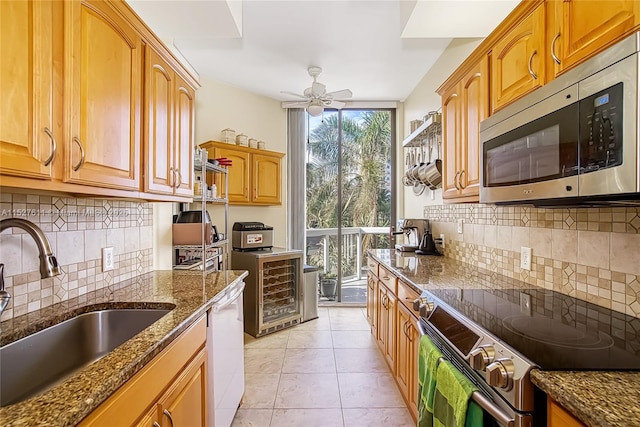 kitchen featuring light tile patterned flooring, appliances with stainless steel finishes, sink, dark stone counters, and ceiling fan