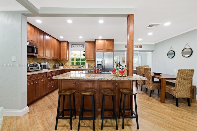 kitchen with light stone countertops, a kitchen breakfast bar, light hardwood / wood-style floors, and appliances with stainless steel finishes