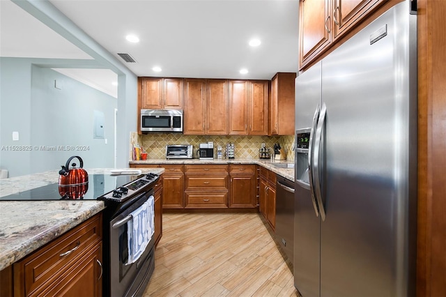 kitchen featuring appliances with stainless steel finishes, light hardwood / wood-style floors, light stone countertops, and tasteful backsplash