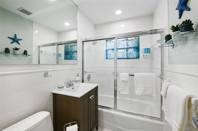 full bathroom with tile walls, toilet, vanity, and shower / bath combination with glass door