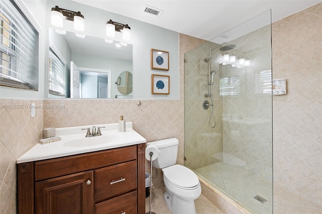 bathroom with tile walls, toilet, a shower with door, tile floors, and vanity