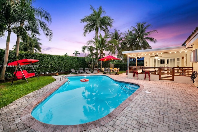 pool at dusk with ceiling fan and a patio