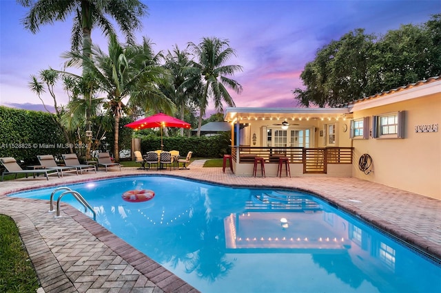 pool at dusk featuring a patio area and ceiling fan