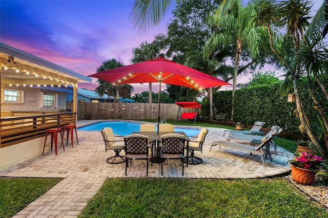 patio terrace at dusk featuring a fenced in pool