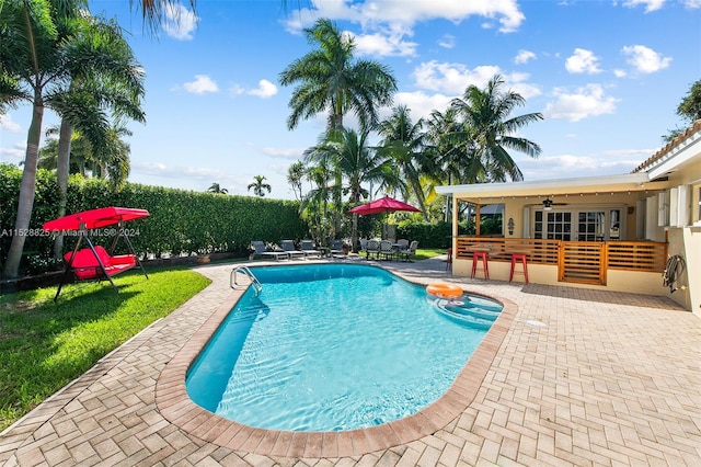 view of swimming pool featuring a lawn, a bar, a patio area, and ceiling fan