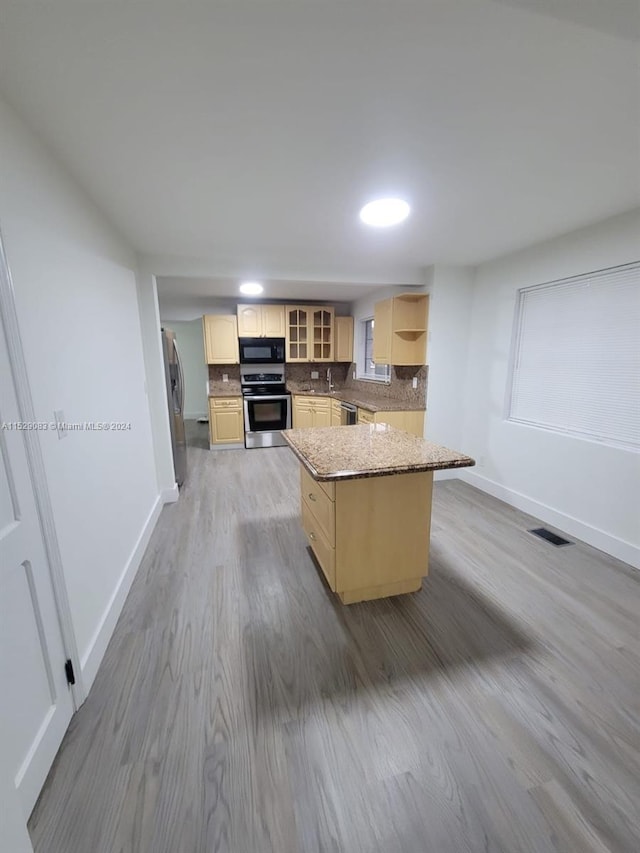 kitchen featuring appliances with stainless steel finishes, tasteful backsplash, light brown cabinets, a center island, and light hardwood / wood-style floors