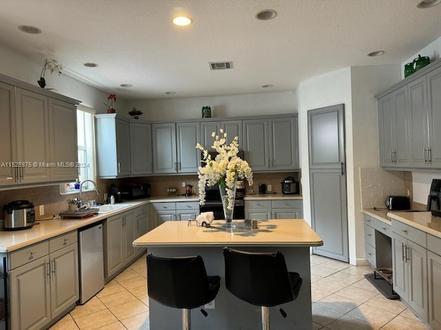 kitchen featuring backsplash, sink, a center island, stainless steel dishwasher, and gray cabinets