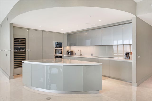 kitchen featuring gray cabinets, oven, beverage cooler, and a spacious island