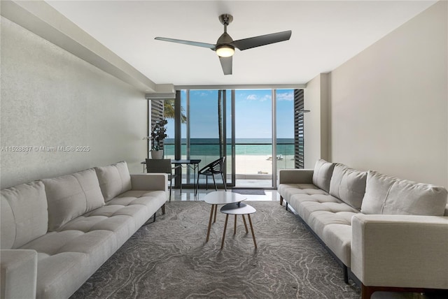 living room featuring floor to ceiling windows, ceiling fan, and a water view