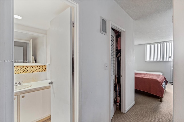 hallway with a textured ceiling, sink, and light colored carpet