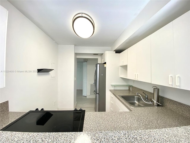 kitchen with white cabinets, stovetop, stainless steel refrigerator, and sink