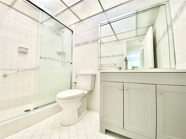 bathroom featuring toilet, a shower with door, vanity, tile walls, and tile flooring