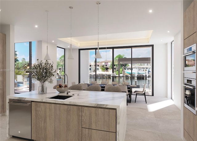 kitchen with a raised ceiling, a water view, sink, and decorative light fixtures