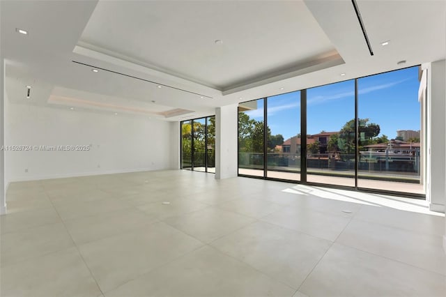 empty room with a raised ceiling, a water view, and expansive windows