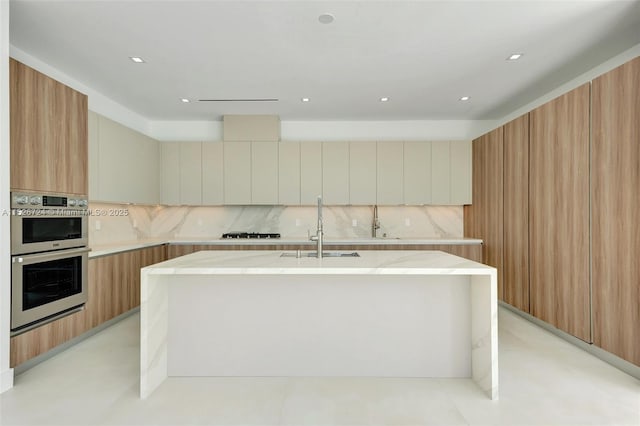 kitchen with stainless steel double oven, tasteful backsplash, white gas cooktop, sink, and a kitchen island with sink