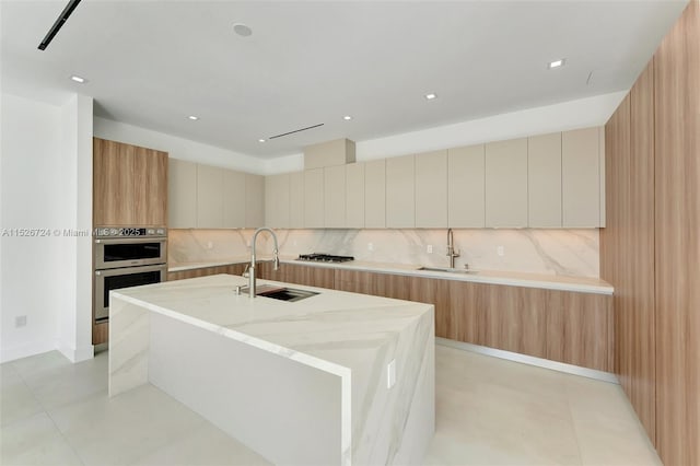 kitchen featuring sink, a center island with sink, light stone countertops, and decorative backsplash