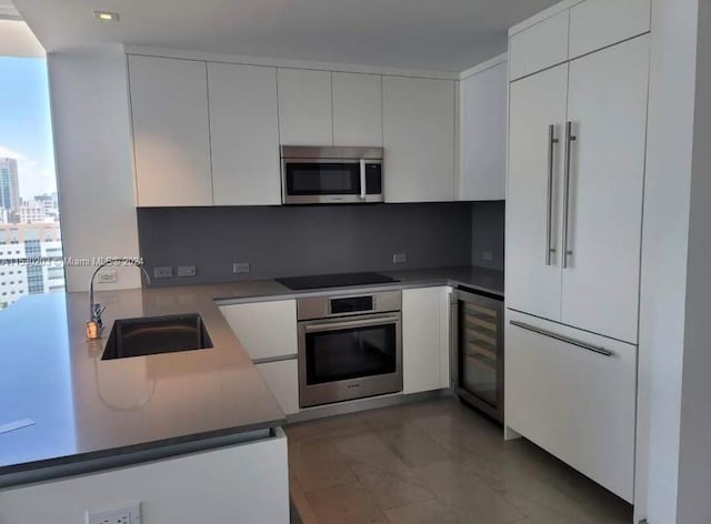 kitchen with appliances with stainless steel finishes, backsplash, white cabinetry, sink, and beverage cooler