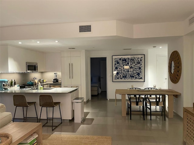 kitchen with a kitchen breakfast bar, sink, light tile patterned floors, white cabinetry, and kitchen peninsula