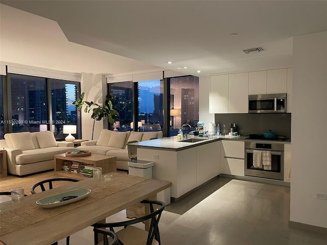 kitchen with a wall of windows, white cabinetry, sink, kitchen peninsula, and stainless steel appliances