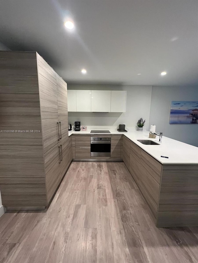 kitchen with light hardwood / wood-style flooring, sink, white cabinetry, and stainless steel oven