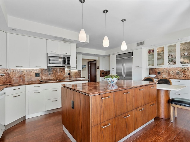 kitchen featuring a kitchen island, appliances with stainless steel finishes, pendant lighting, white cabinetry, and dark wood-type flooring