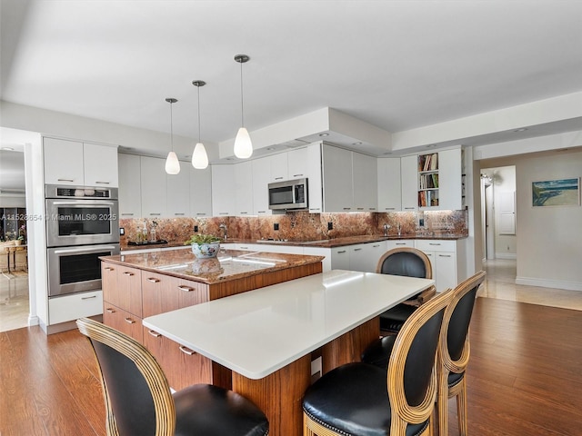 kitchen with white cabinetry, hanging light fixtures, stainless steel appliances, a kitchen island, and dark hardwood / wood-style flooring