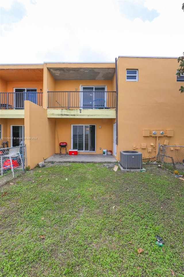 rear view of house with a balcony, a yard, central AC, and a patio area