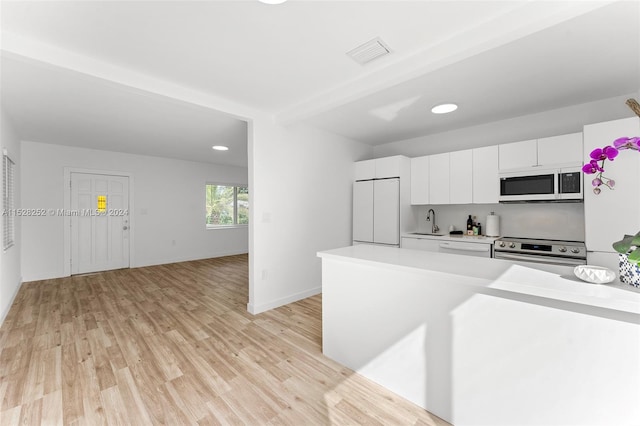 kitchen with appliances with stainless steel finishes, white cabinets, sink, light wood-type flooring, and beam ceiling