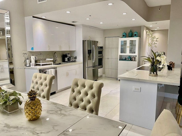 kitchen featuring stainless steel appliances, white cabinetry, light stone countertops, and sink