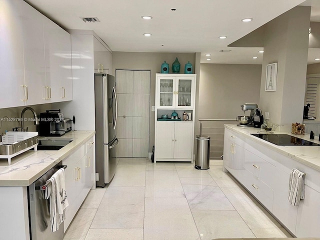 kitchen with white cabinetry, light stone counters, stainless steel fridge, and dishwashing machine