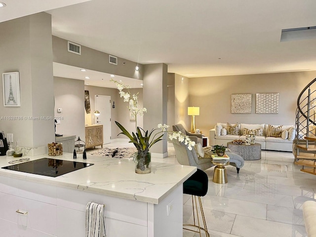 kitchen with light stone counters, white cabinets, black electric cooktop, light tile flooring, and a kitchen bar