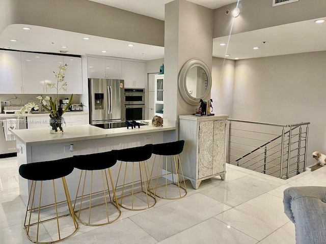 kitchen with a kitchen breakfast bar, white cabinets, appliances with stainless steel finishes, and light tile floors