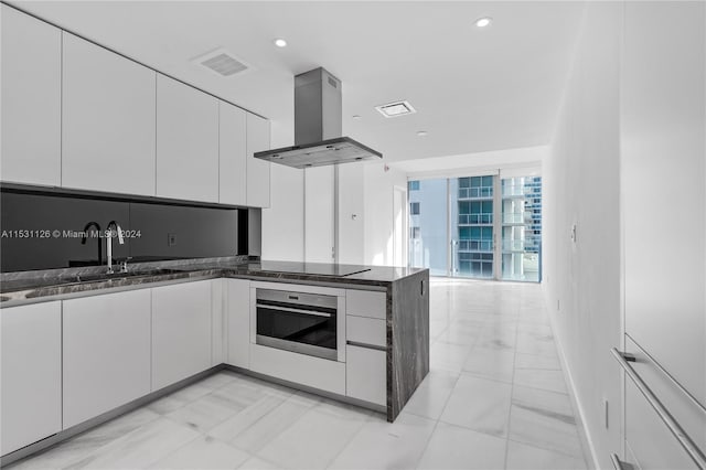 kitchen with light tile floors, island exhaust hood, black electric cooktop, white cabinetry, and stainless steel oven