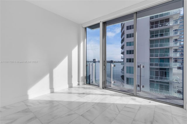 unfurnished room featuring light tile floors, floor to ceiling windows, and a water view