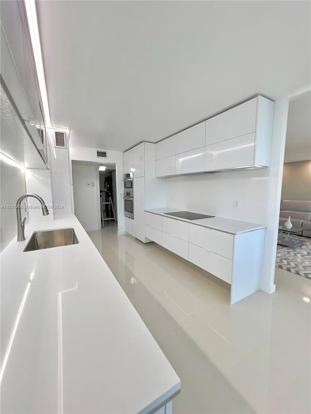 kitchen with white cabinets, sink, black electric stovetop, and double oven