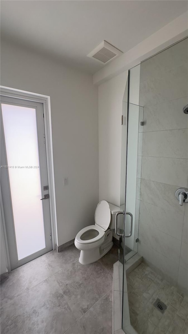 bathroom featuring a shower with door, tile flooring, and toilet