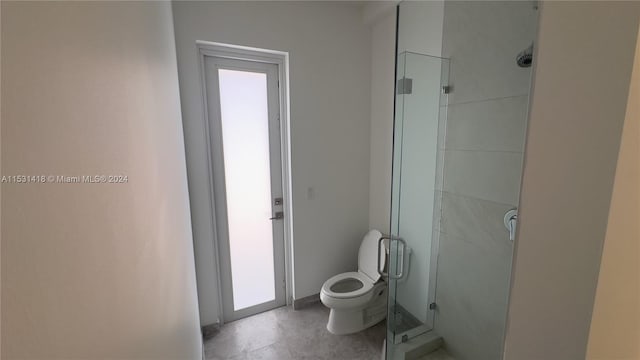 bathroom featuring a shower with door, tile flooring, and toilet