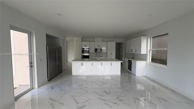 kitchen featuring stainless steel appliances, plenty of natural light, light tile floors, and a kitchen island with sink