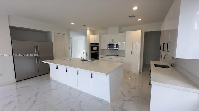 kitchen with appliances with stainless steel finishes, sink, light tile flooring, and an island with sink