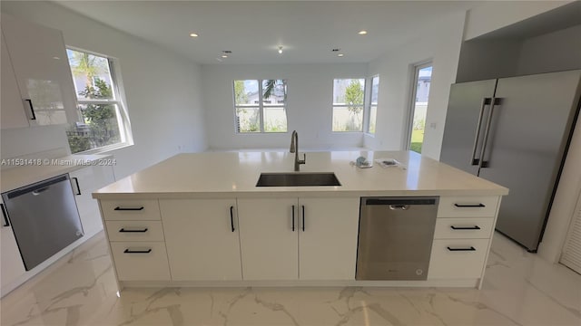 kitchen featuring an island with sink, light tile flooring, sink, white cabinets, and appliances with stainless steel finishes